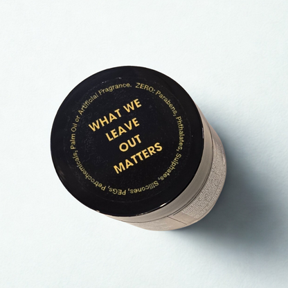 Cosmetics jar with black lid and amber glass jar on a light gray background. On the lid is written in yellow "What we leave out matters"